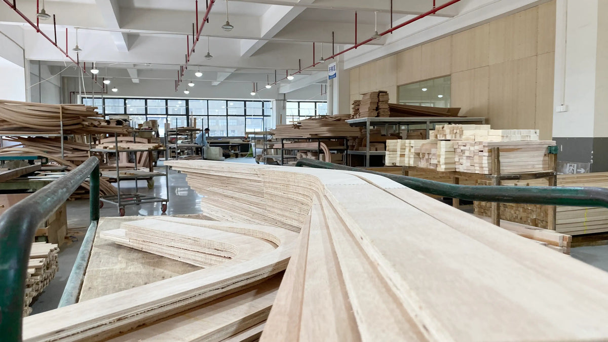 Wooden panels stacked in a warehouse with large windows and industrial equipment.
