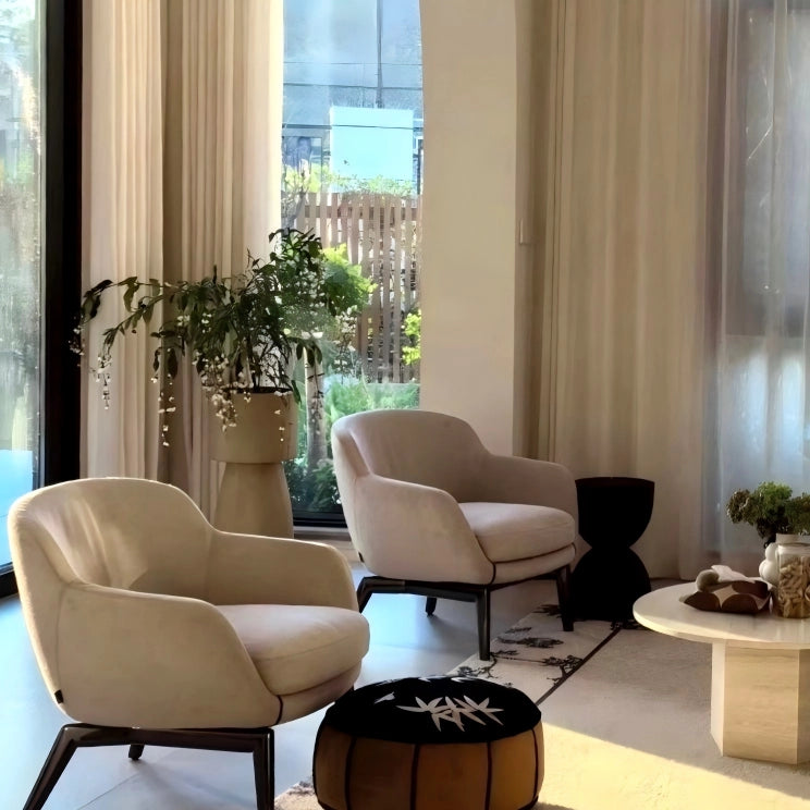 Modern living room with beige armchairs, a coffee table, and decorative items.
