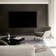 Modern living room with a gray armchair, coffee table, and television on a dark wall.